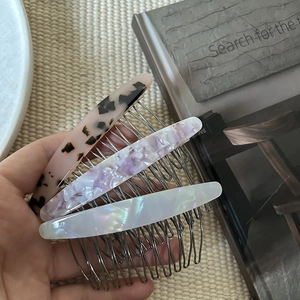 Three acetate hair combs with tortoise and marble patterns on textured book background