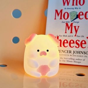 Cute pig shaped night light in warm yellow glow on bookshelf with English book