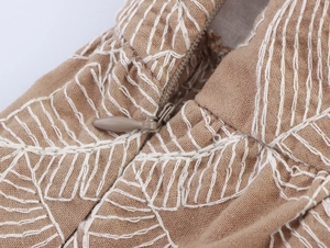 Detail of white embroidery on brown wide-leg pants with high-quality zipper closure