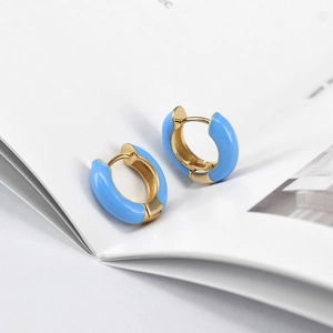 Close-up of sky blue enamel hoop earrings with gold finish on white book pages