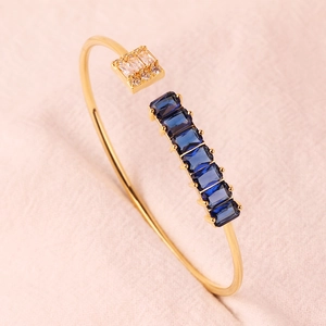 Detailopname van de gouden open armband met blauwe rechthoekige stenen en glanzende zirkoon