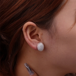 Close-up of silver textured oval stud earring worn by a model in a natural setting