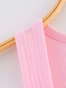 Close-up of sewing details on a pink ribbed knit camisole hanging on a wooden hanger
