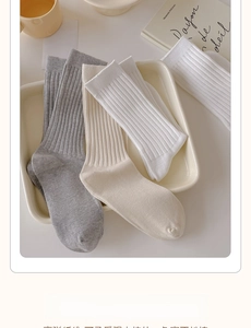 Close-up of ribbed cotton crew socks in grey, cream, and white on a minimalist tray