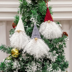 Three Christmas gnomes with knitted hats in white, red and grey hanging on a snowy tree