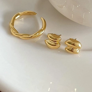 Detailed view of polished golden geometric stud earrings and a twisted open ring set