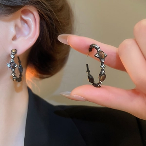 Close-up of vintage C-shaped black earrings with crystals and brown tiger eye stones