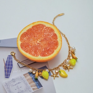 Detailed close-up of 18K gold chain with lemon, star, and pearl charms for summer style