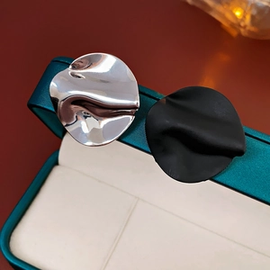 Close-up of asymmetric wavy round stud earrings in silver and black on a green jewelry box