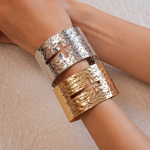 Close-up of gold and silver textured metal cuff bracelets with hollow cross design