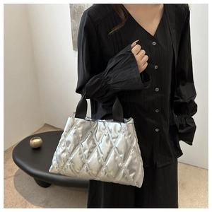 Detail of silver quilted tote bag featuring a padded texture and black fabric handles