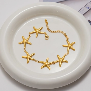 Close-up of gold starfish bracelet with freshwater pearls on a white ceramic plate