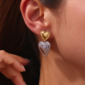 Macro detail of double-layered heart stud earrings in gold and silver finish