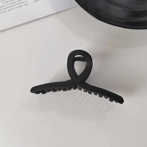 Vue de dessus d'une pince à cheveux noire mate avec un design croisé minimaliste fluide