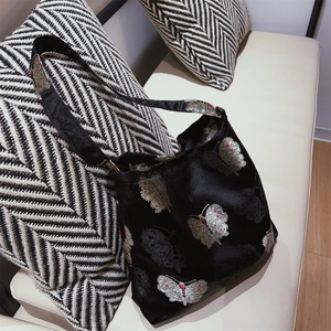 Close-up of black satin shoulder bag featuring colorful butterfly embroidery on a cushion