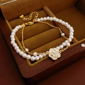 Detailed close-up of double-layer gold pearl bracelet with camellia charms on wood box