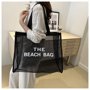 Detail of the large black mesh tote bag with THE BEACH BAG logo on the shoulder