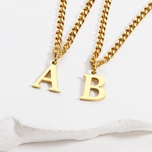 Close-up of 18K gold plated A and B initial pendants on Cuban chains over white stone