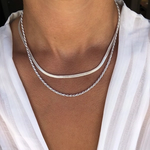 Close-up of layered silver stainless steel herringbone and rope chains on a neck