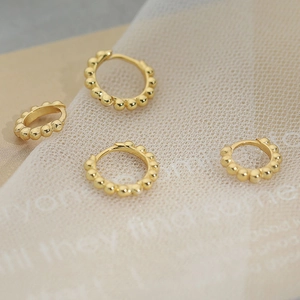 Elegant gold beaded hoop earrings in S925 silver displayed on textured fabric