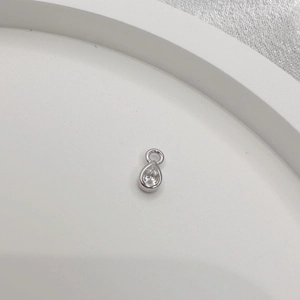Macro shot of silver teardrop charm with clear zircon bezel setting on white tray