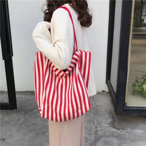 Detail view of large red and white striped canvas tote bag worn by a model on the shoulder