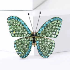 Close-up of butterfly brooch with green and blue rhinestones on white geometric background