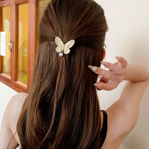 Detailed view of a golden butterfly hair clip with pearl pendant on long hair