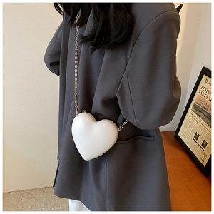 Detail shot of a white heart-shaped crossbody bag with a sleek gold chain strap on a model