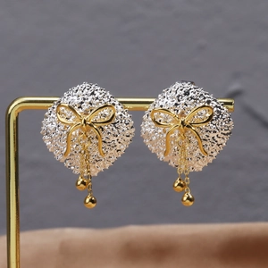 Detail of silver textured disc earrings with golden bow and elegant fringe tassel
