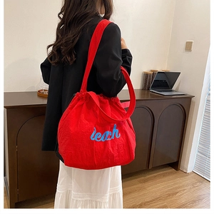 Detail view of red drawstring canvas tote bag with blue Yeah print shown on shoulder