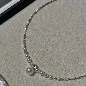Elegant silver chain necklace with pearls and a large pearl pendant on beige linen