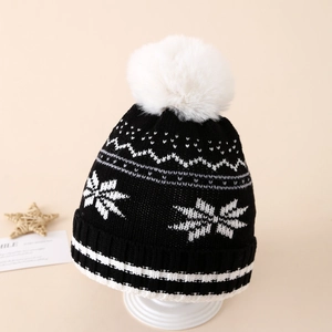 Detailed texture of black winter knit hat with white snowflakes and large faux fur pompom