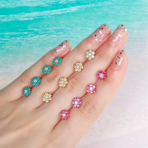 Floral zircon stud earrings in blue yellow and pink displayed on a beach background