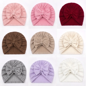 Knitted baby turban hats with bow detail shown in nine colors on a white background