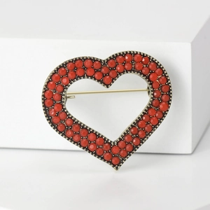 Vintage heart shaped brooch with red beads and antique bronze metal frame on white surface