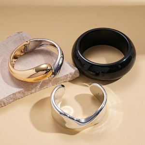 Three minimalist geometric bangles in gold, silver, and black on a textured stone base