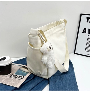 Detail of off-white canvas messenger bag with adjustable strap and cute plush bear charm