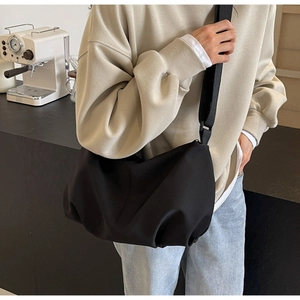 Detail of black cloud-style nylon crossbody bag worn by model in a café setting