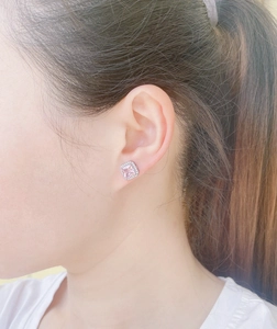 Close-up of pink square-cut ruby stud earring worn on ear with halo diamond accents