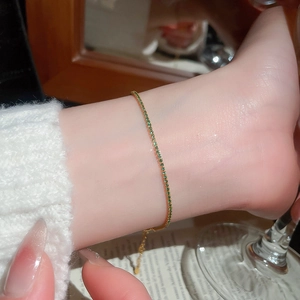 Close-up of a gold tennis bracelet featuring small green cubic zirconia stones on a wrist