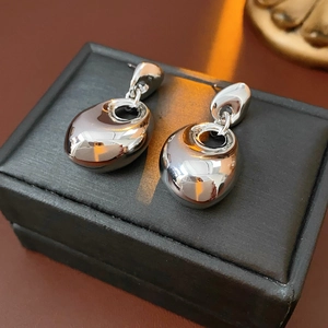Macro shot of silver irregular oval drop earrings on a black textured jewelry box