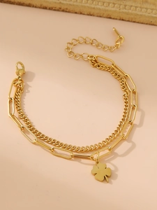 Détail d'un bracelet doré double couche avec chaîne gourmette et pendentif trèfle