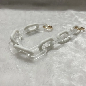 Detail of matte white and frosted acrylic chain link accessory with gold metal ring