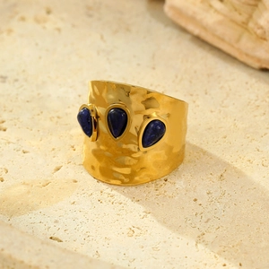 Detailed close-up of a wide gold ring with hammered texture and three blue teardrop gems