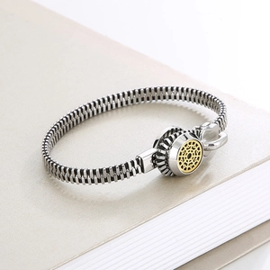 Detail of silver zipper bracelet with gold round charm on grey book background