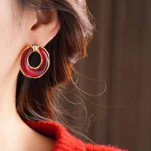 Close-up of a burgundy resin hoop earring with a golden metal clasp on a female model