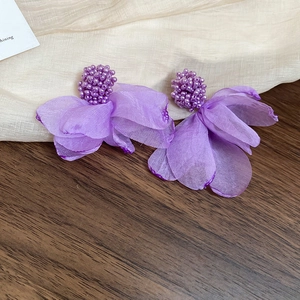 Close-up of purple fabric flower earrings with beaded clusters on a neutral fabric base