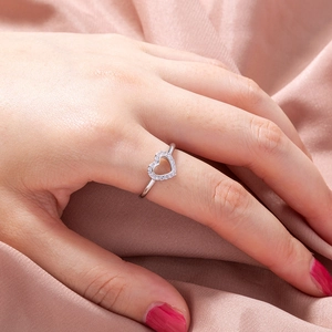 Close-up of heart-shaped zircon ring on pink silk fabric with delicate silver band
