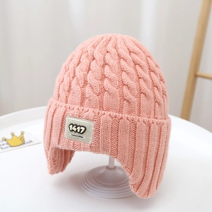 Detail of pink cable knit hat with a fashion label on a white display stand